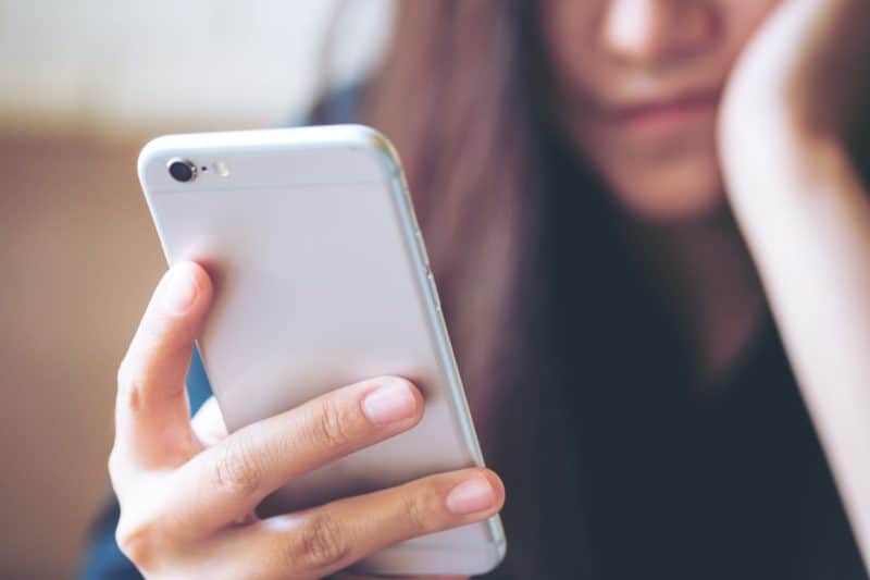 Beautiful Asian girl using smart phone in modern cafe with feeling bored